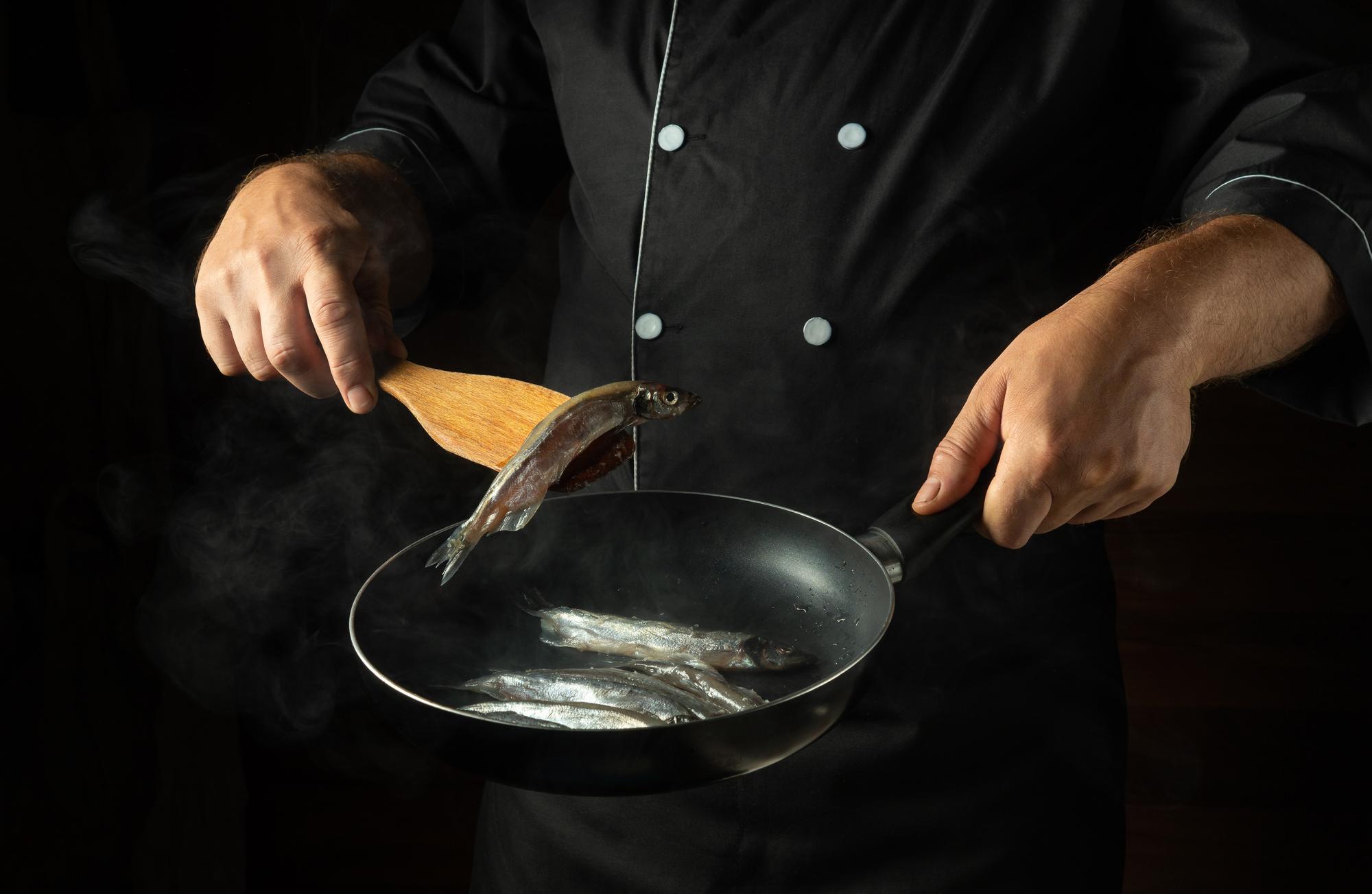 Hands searing a piece of fish on a hot pan